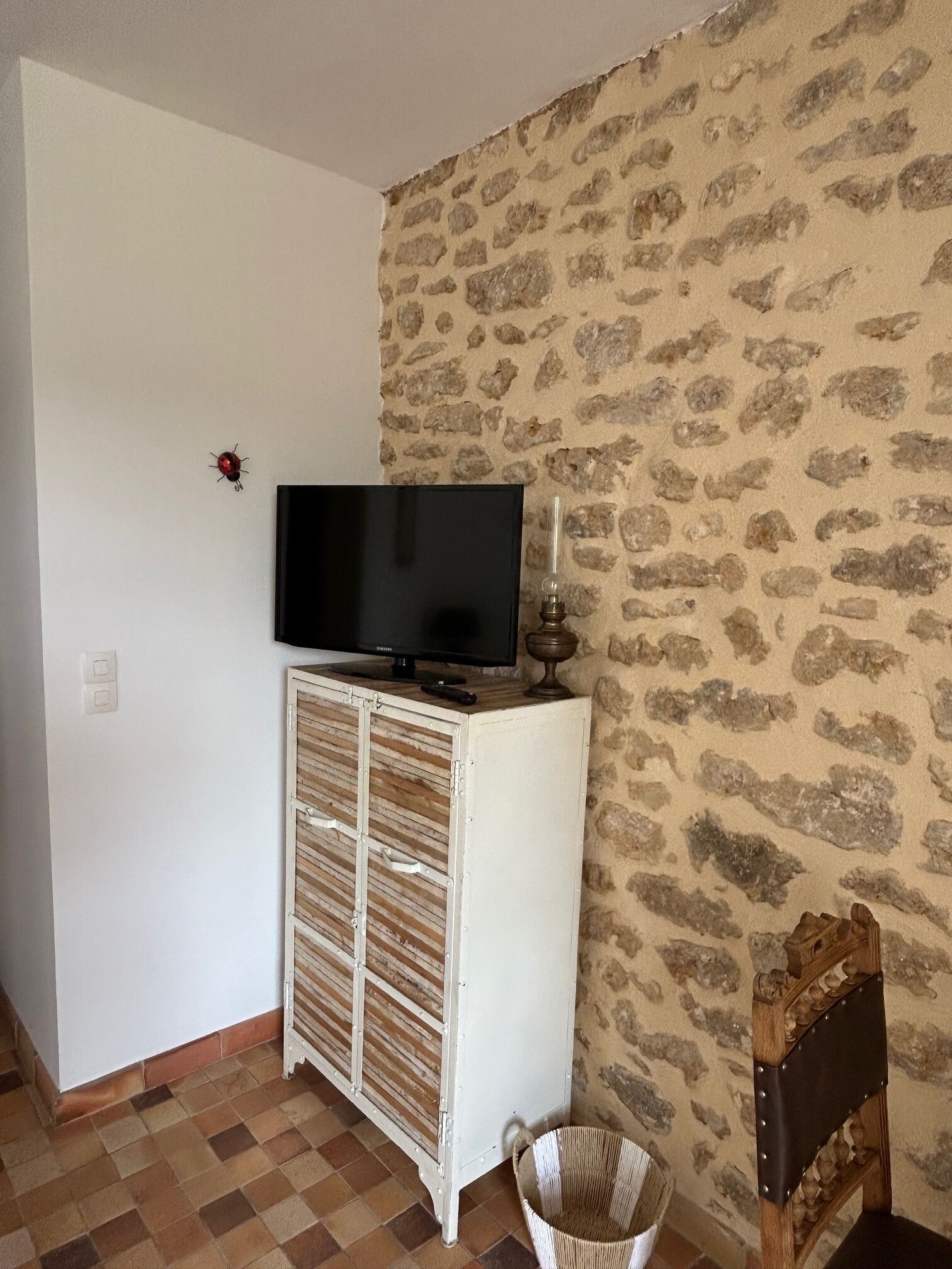 A room with a television on a white cabinet, a stone-patterned wall, and a tiled floor.
