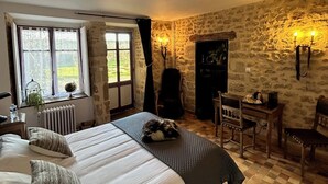 Una habitación acogedora con cama, escritorio y silla. Se observa una ventana con cortinas, un radiador y una pared de piedra.