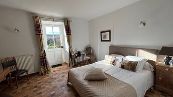 A bedroom with a large bed, a chair, a desk, and a view through a window.