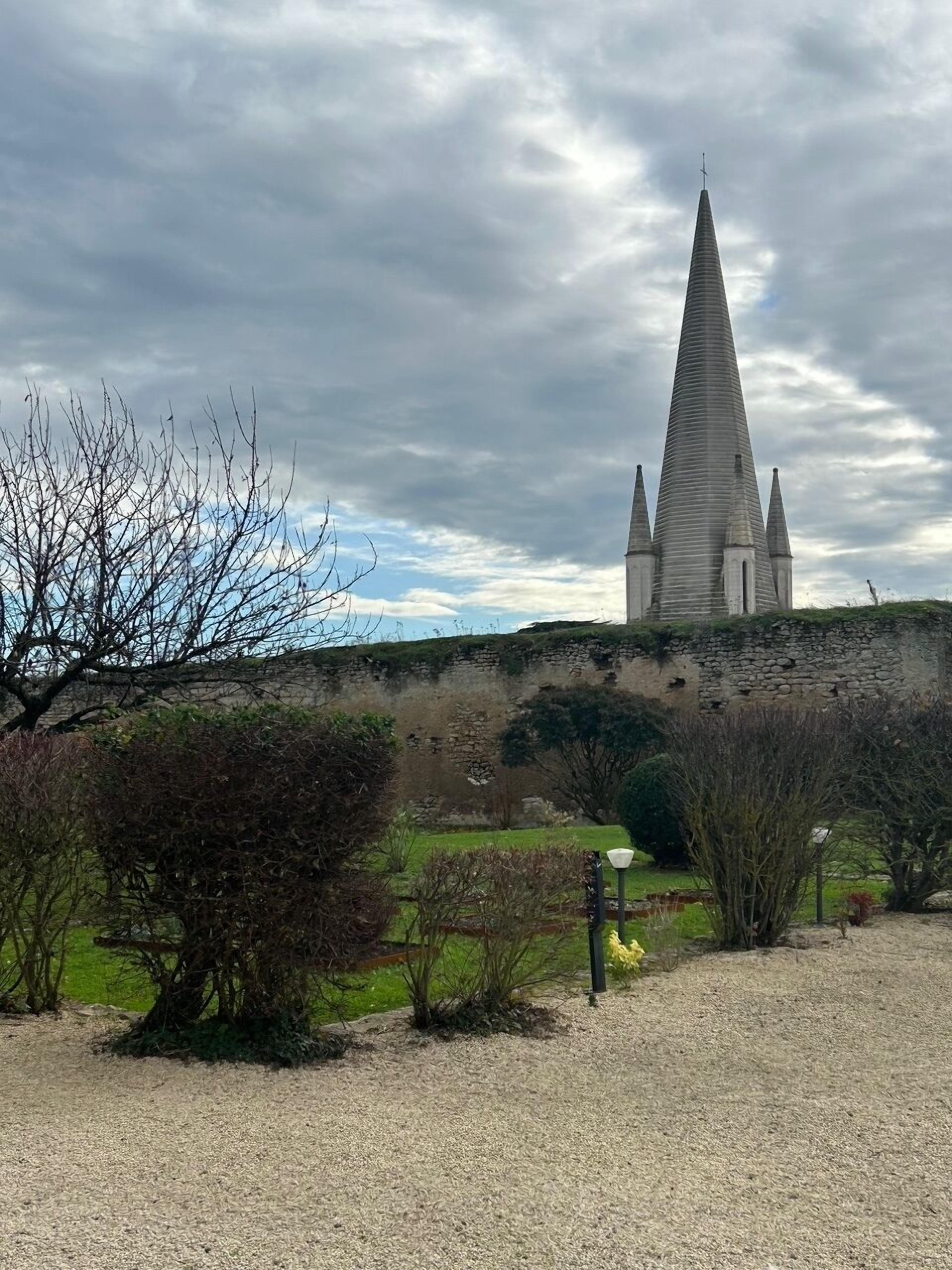 Una iglesia con una aguja alta y un muro de piedra al fondo.