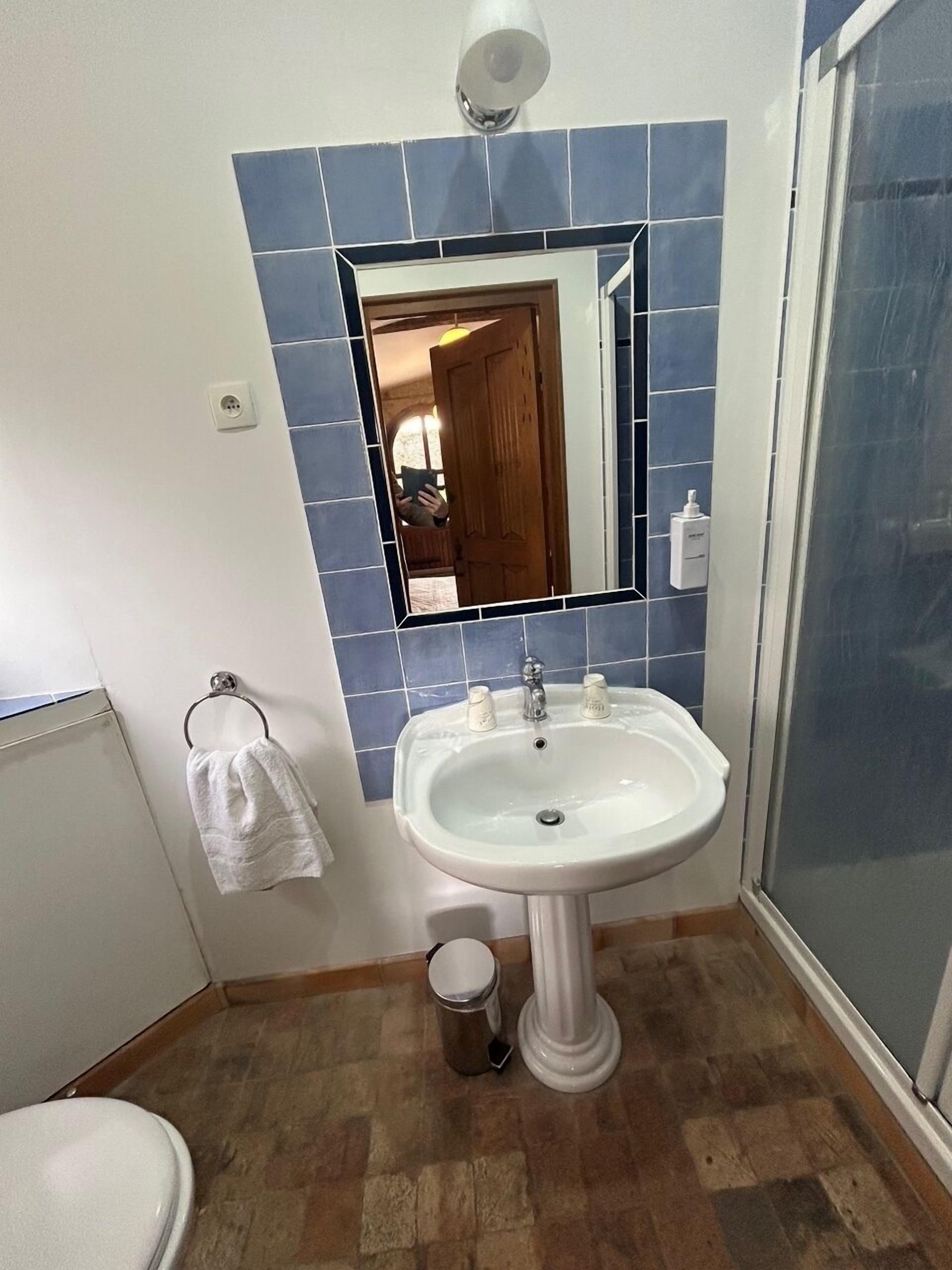 A bathroom with a white sink, blue-tiled walls, a mirror, and a shower.