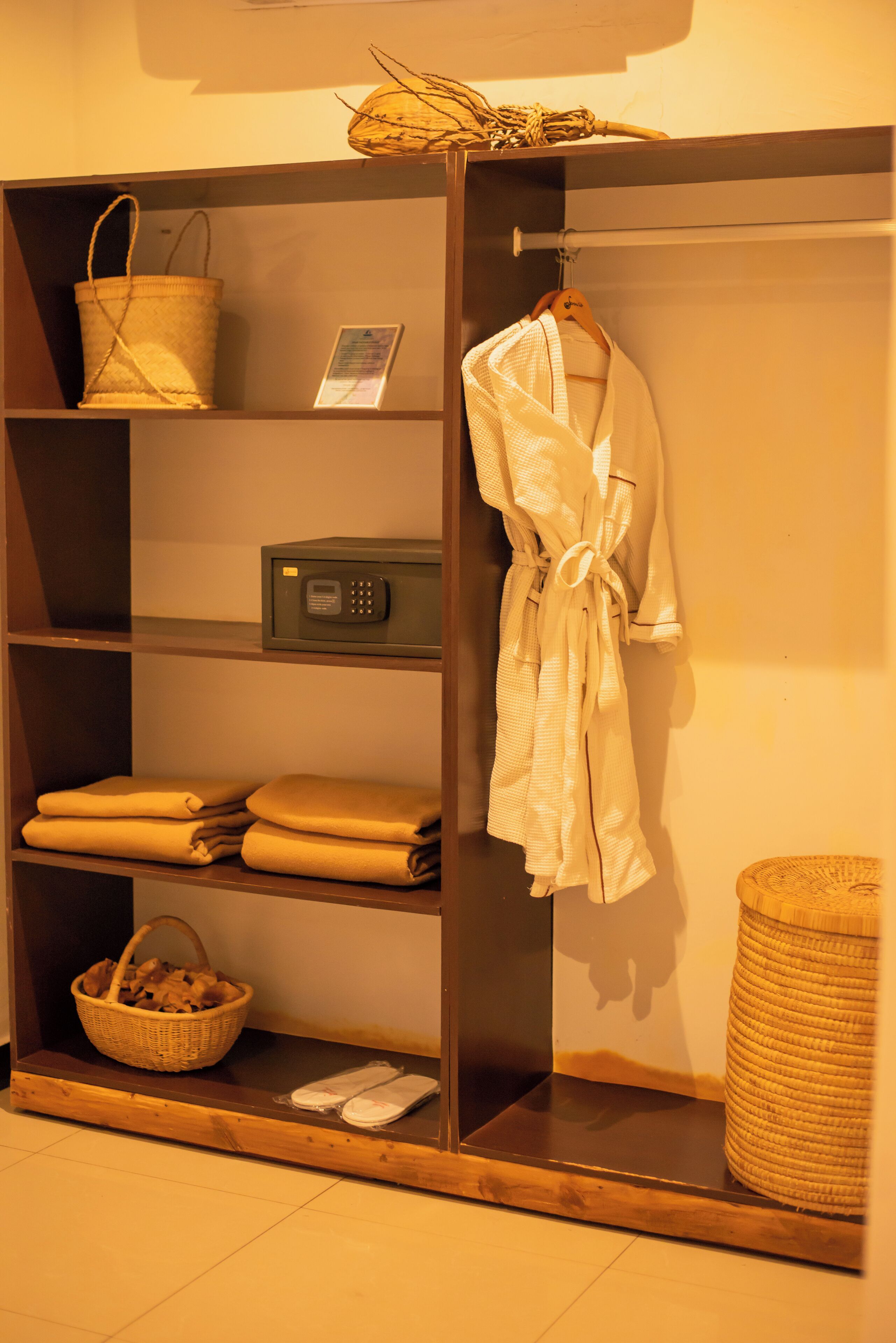 Ein hölzerner Kleiderschrank mit Regalen, der gefaltete Handtücher, einen Bademantel, einen Korb und eine Mikrowelle beherbergt.