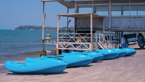 Una struttura in legno con tetto di paglia e un molo che si estende sull'acqua, dove sono allineate diverse canoe blu.