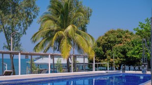 Una piscina con bordo piastrellato, circondata da palme e un edificio con tetto blu.