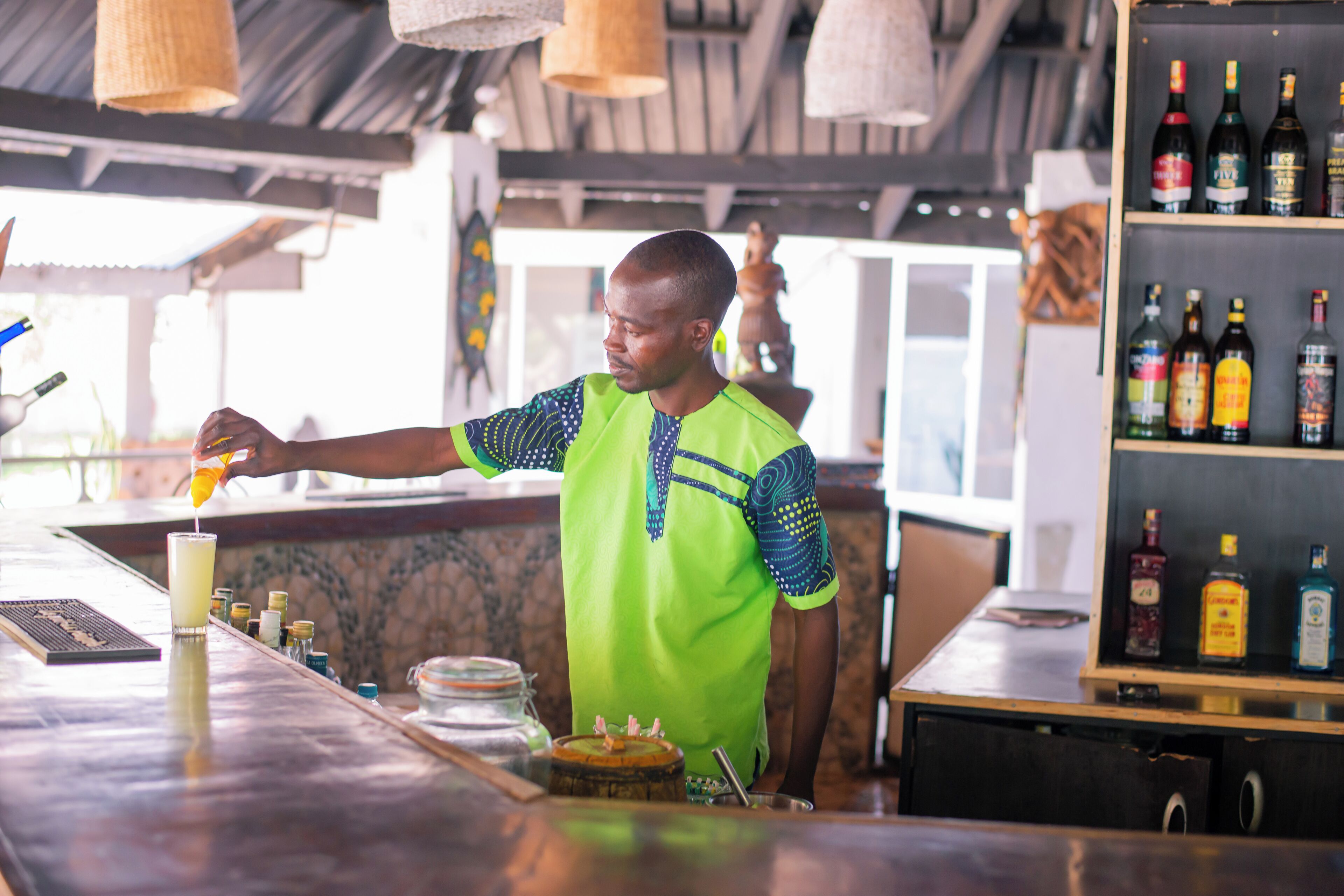 Ein Barkeeper bereitet ein Getränk an einer Bar mit Holzboden und Regalen voller Spirituosen zu.