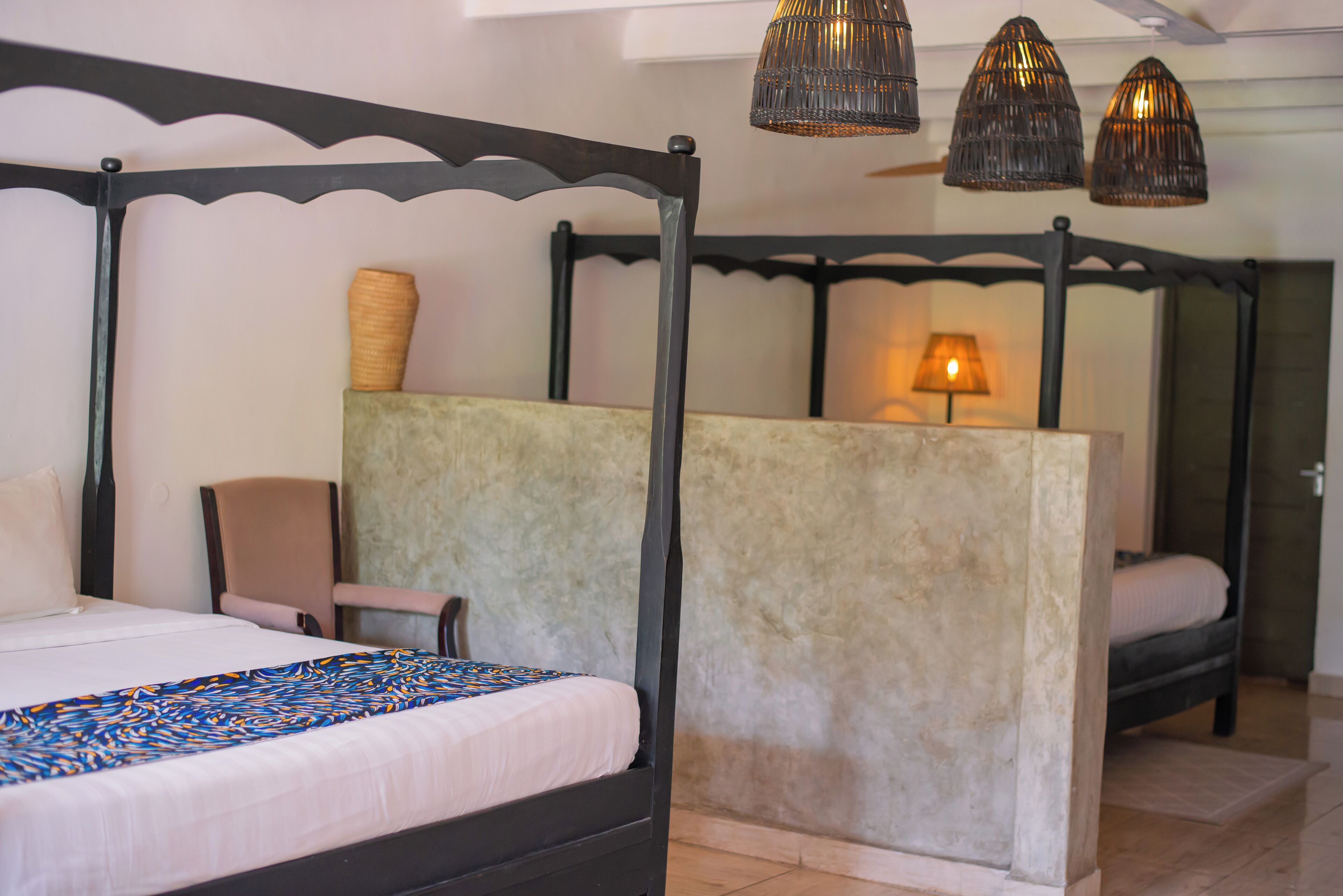 A four-poster bed with a headboard, a bedside table with a lamp, and a chair.