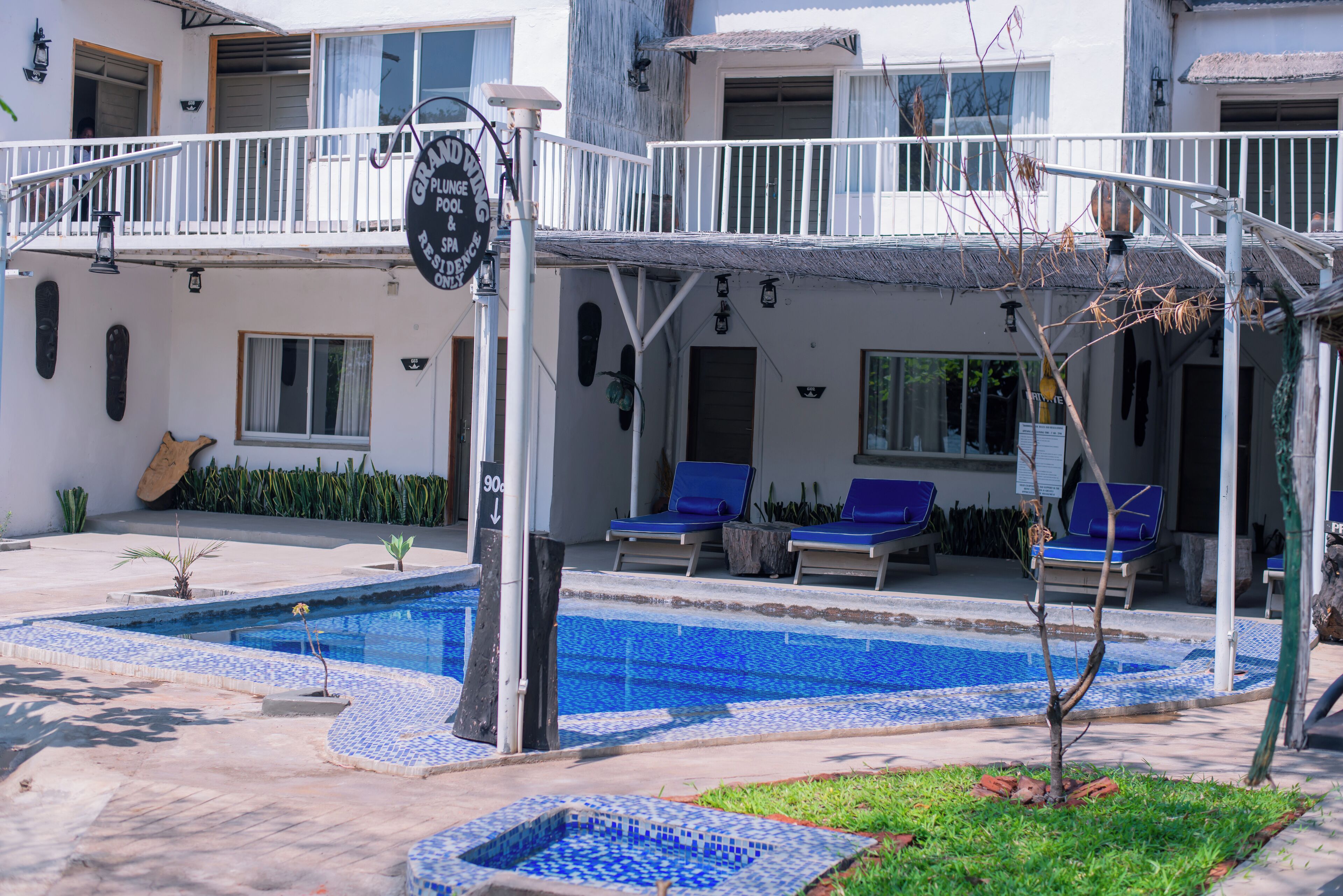 Un hotel con piscina, sillones reclinables azules y un balcón con barandilla.