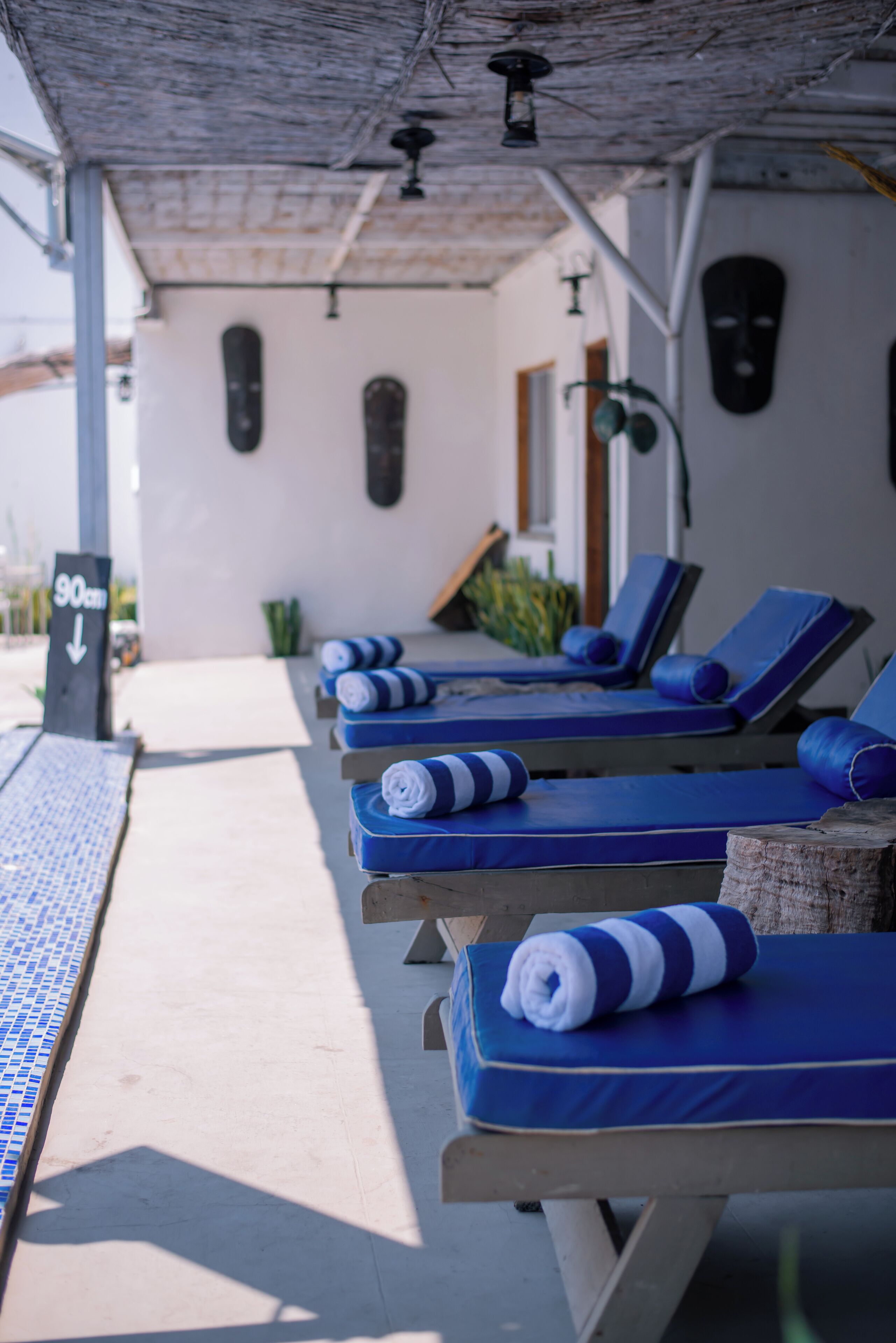 A row of sun loungers with blue cushions and striped towels, a tiled floor, and a sign indicating a 90-degree angle.