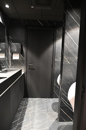 A modern bathroom with a dark marble floor, a sink, and a toilet. - Bremberg Hotel (Bierbeek)