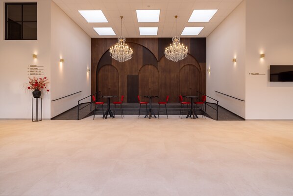 Un hall d’entrée spacieux au design moderne, avec un escalier central, des fauteuils rouges, des lustres et des panneaux de signalisation.