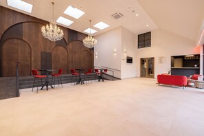 Un vestíbulo amplio con una lámpara moderna, sillas rojas y una zona de recepción.