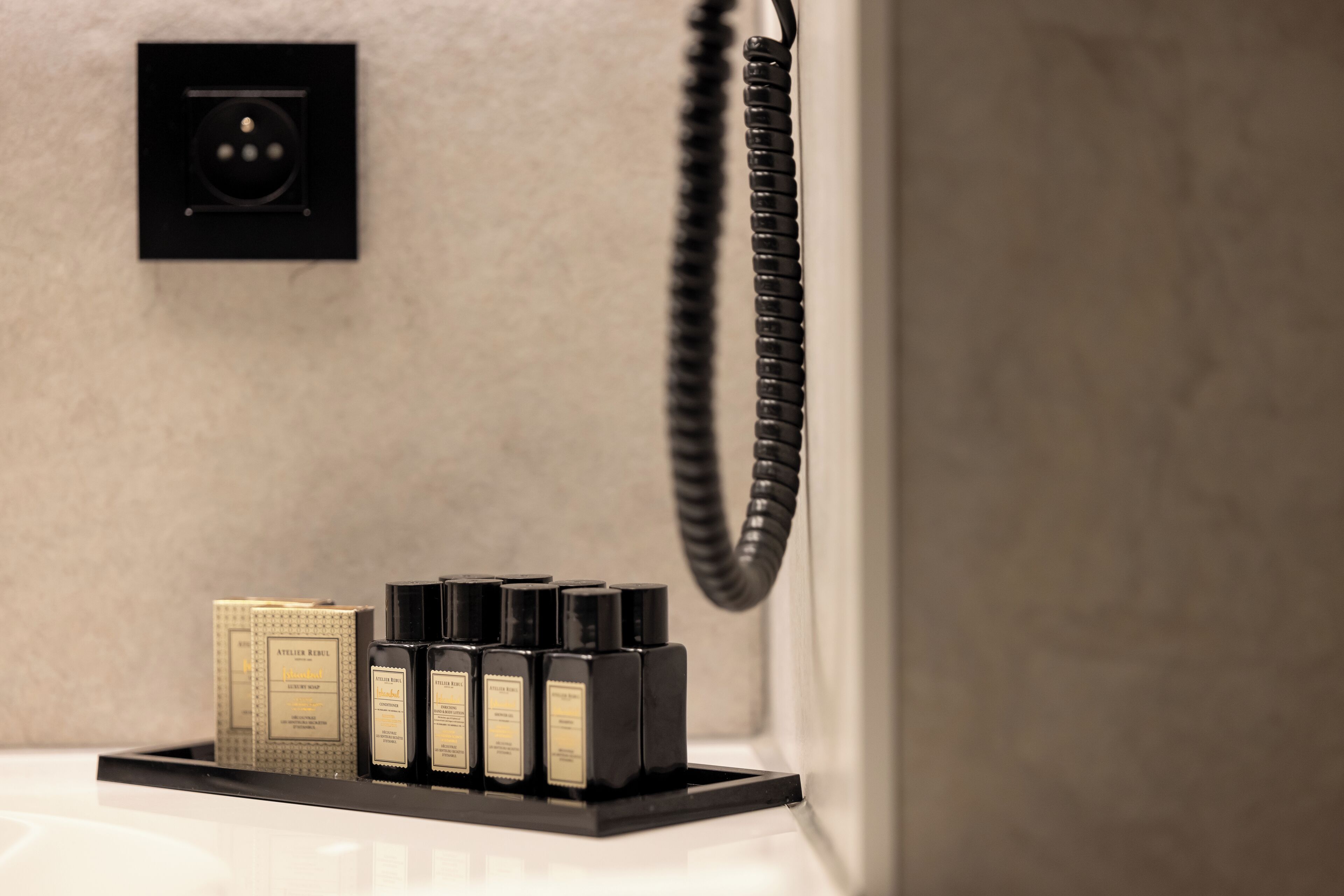 A bathroom with a black telephone, a black charging station, and a set of toiletries on a tray.