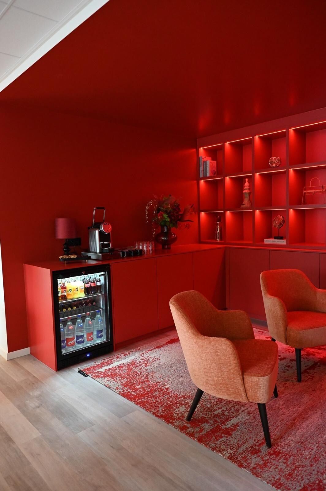 A modern room with a red color scheme, featuring a minibar, two orange chairs, and a red carpet.