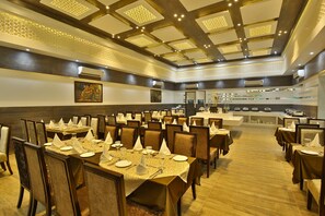 Un vaste espace dédié à la salle à manger, avec de nombreuses tables dressées pour accueillir les convives, agrémenté d’un design moderne au niveau du plafond et d’un buffet central.