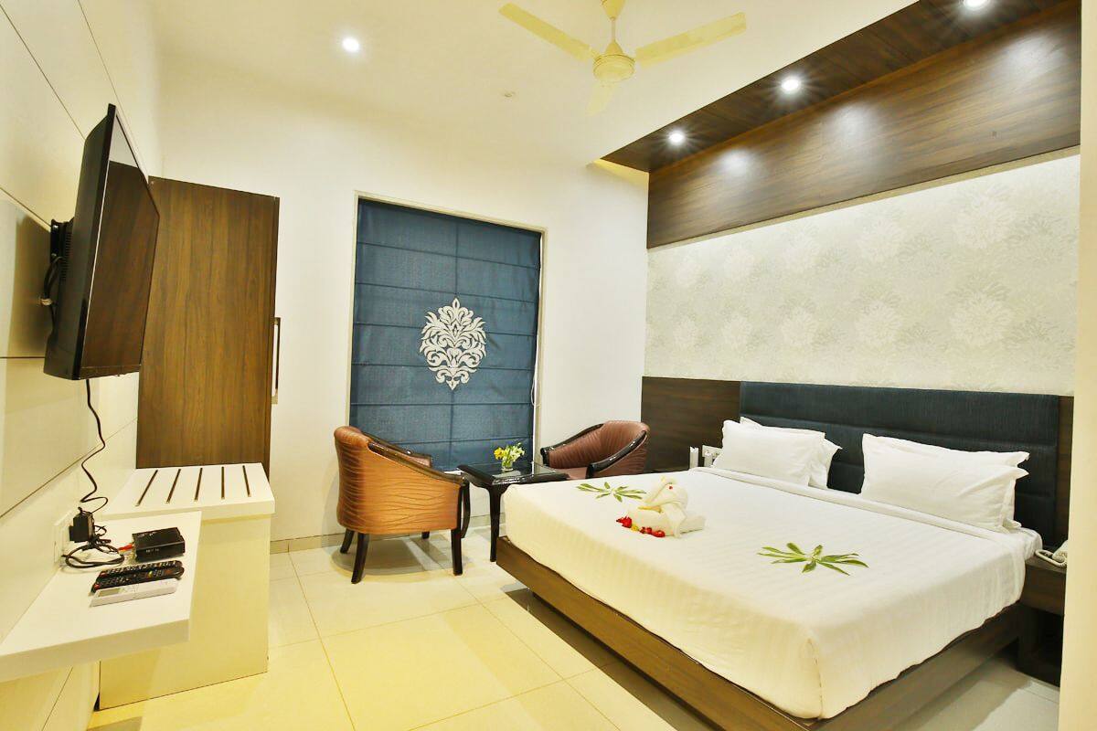 A modern hotel room with a large bed, a flat-screen TV, a desk with a computer, and a chair.