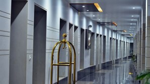 Un pasillo moderno de hotel con piso reflectante, un ascensor dorado y varias puertas a lo largo de las paredes.