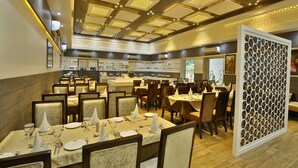 Un restaurante espacioso con varias mesas y sillas, una zona de bar central y un techo decorativo con iluminación empotrada.
