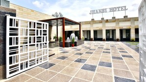 Una entrada de hotel con un patio empedrado, un espacio de descanso cubierto y plantas en macetas.
