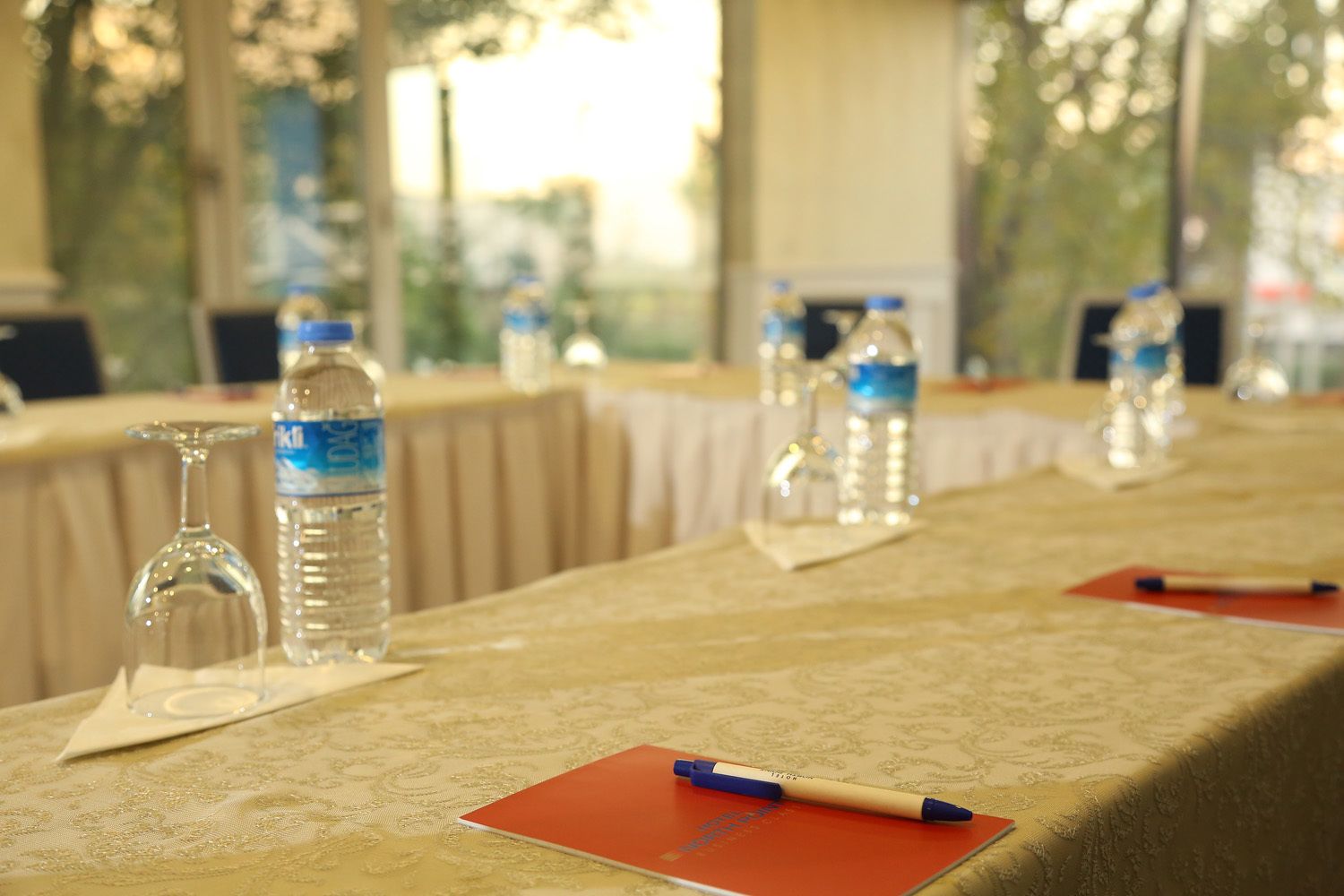 Una mesa servida con botellas de agua, vasos y un bloc de notas con un bolígrafo.