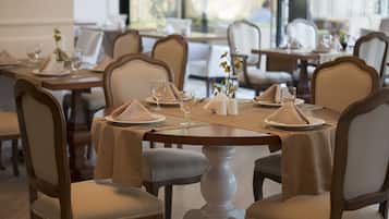 Un comedor con mesas redondas, sillas color beige y mesas cuidadosamente dispuestas con platos, vasos y servilletas.