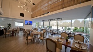 Un comedor amplio con varias mesas y sillas, una pantalla de televisión y ventanas grandes que ofrecen vistas al exterior.