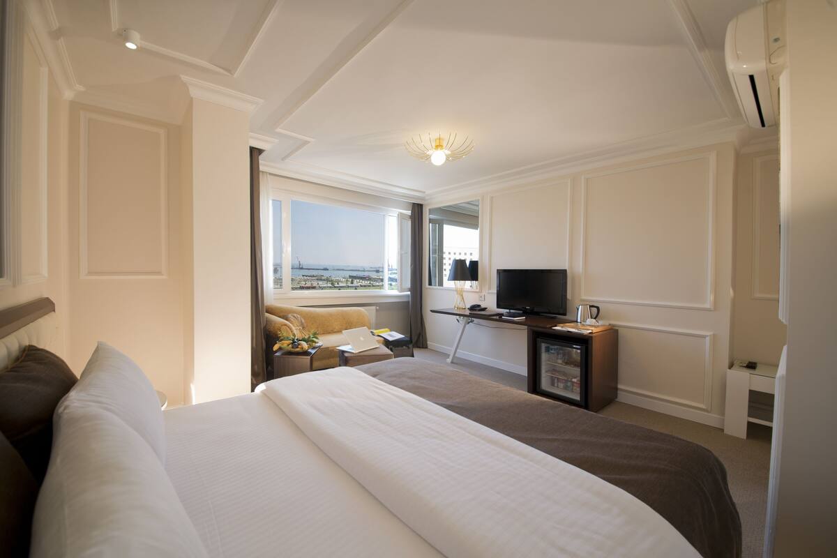 A hotel room with a large bed, a desk with a computer, a television, and a view of the city through the window.