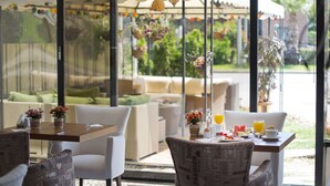 Un comedor con asientos al aire libre, que incluye una mesa con una bebida y un plato de comida, y un sofá con cojines.