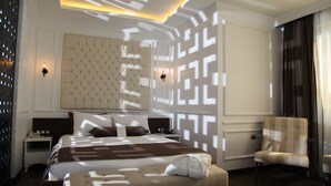 Una habitación de hotel moderna con una cama grande, un cabecero capitonado, dos mesitas de noche y una silla.