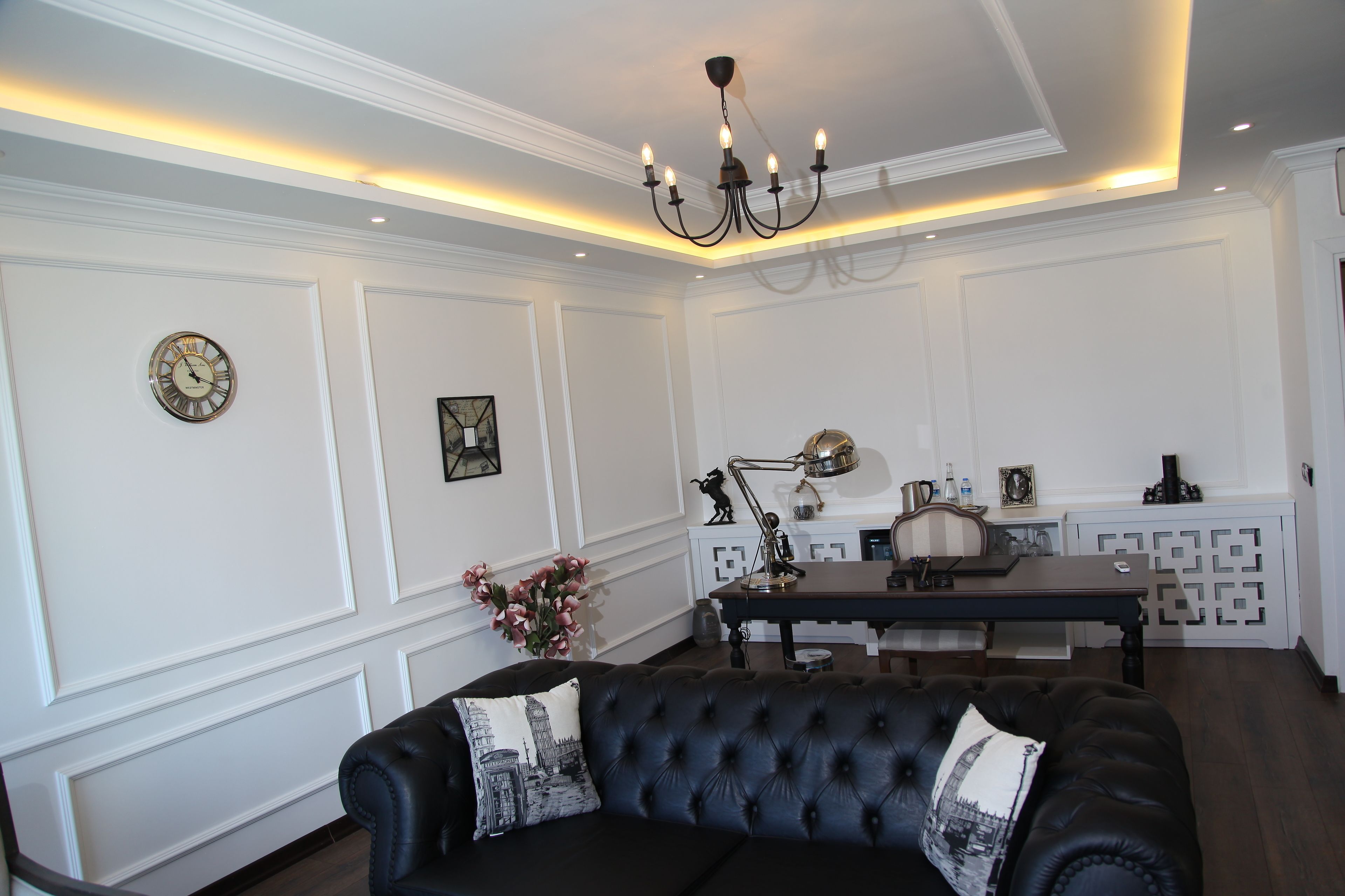 A living room with a black leather sofa, a chandelier, and a dining area with a table and chairs.