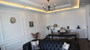 A living room with a black leather sofa, a chandelier, and a dining area with a table and chairs.