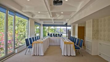 A conference room with a long table, blue chairs, and large windows offering a view of greenery.