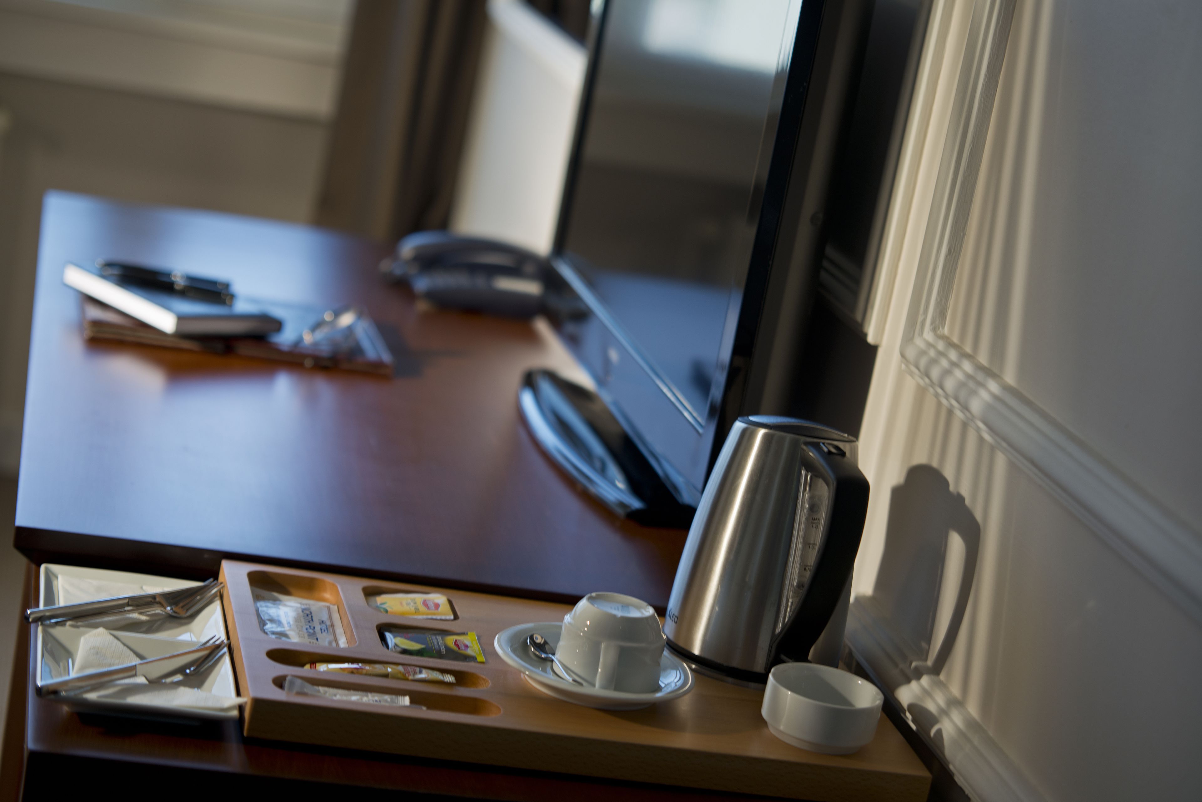 Escritorio de hotel con una taza de café, un teléfono inteligente, un cuaderno y una taza de té.