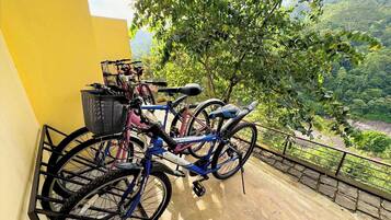 A balcony with bicycles, a metal basket, and a view of a green landscape.