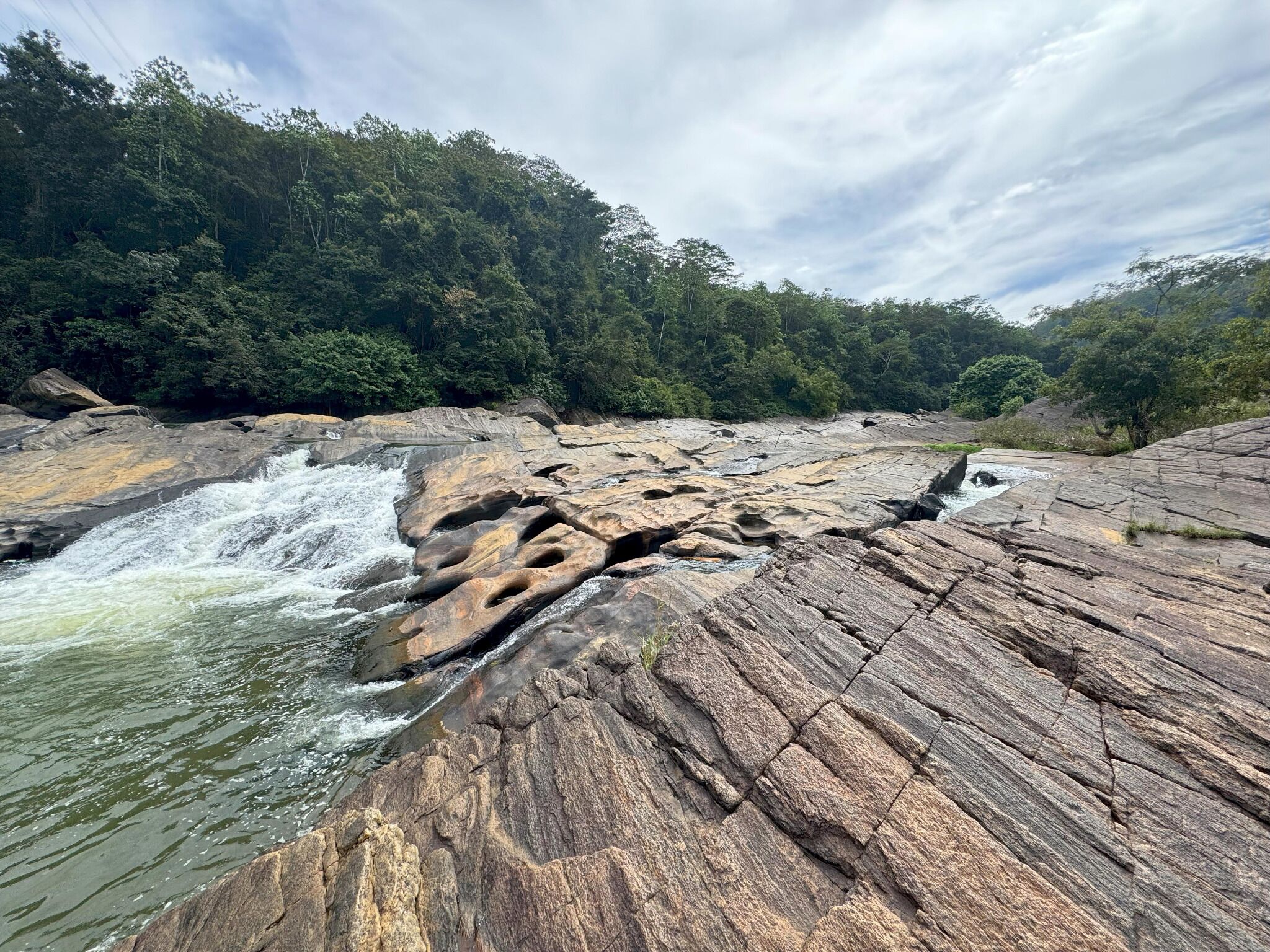 A natural landscape with a rocky riverbed and a forested hillside.