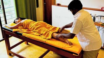 A massage therapy room with a wooden table, a person receiving a massage, and a small table with bottles in the background.