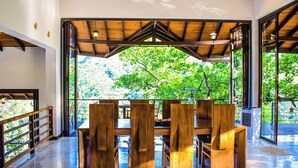 A spacious room with a large wooden table and chairs, a telescope, and a view of lush greenery outside. - Aqua Dunhinda Villa & Nature Retreat (Kandy)