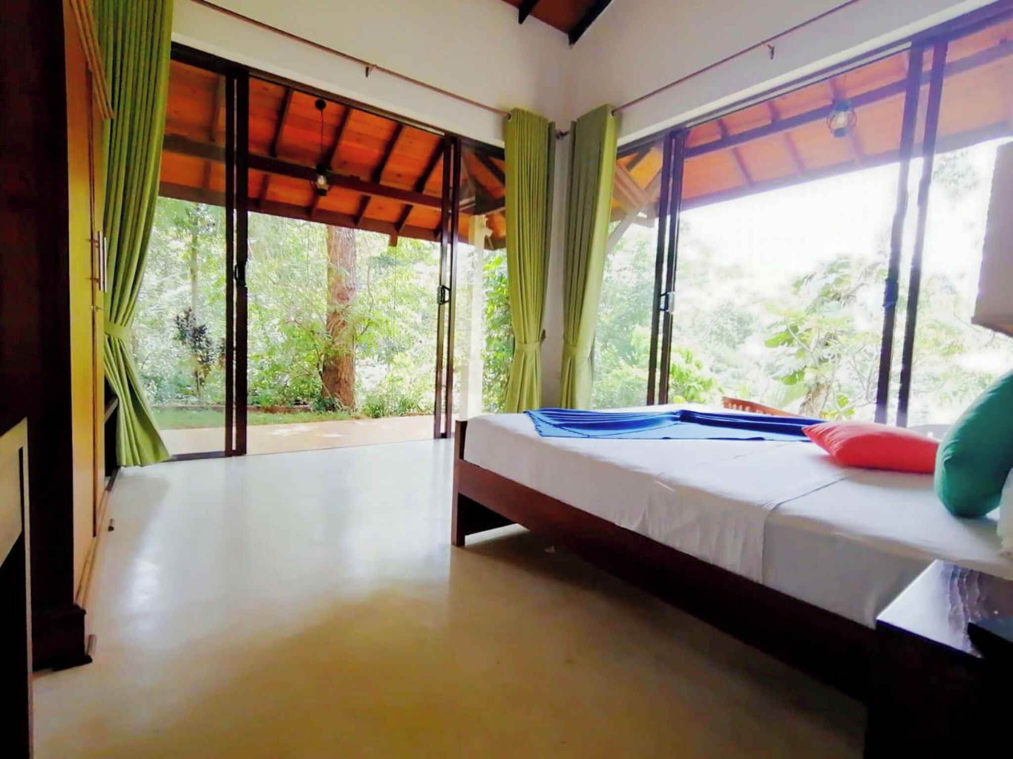 A room with a bed, large windows, and a view of greenery outside.