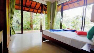 A room with a bed, large windows, and a view of greenery outside.