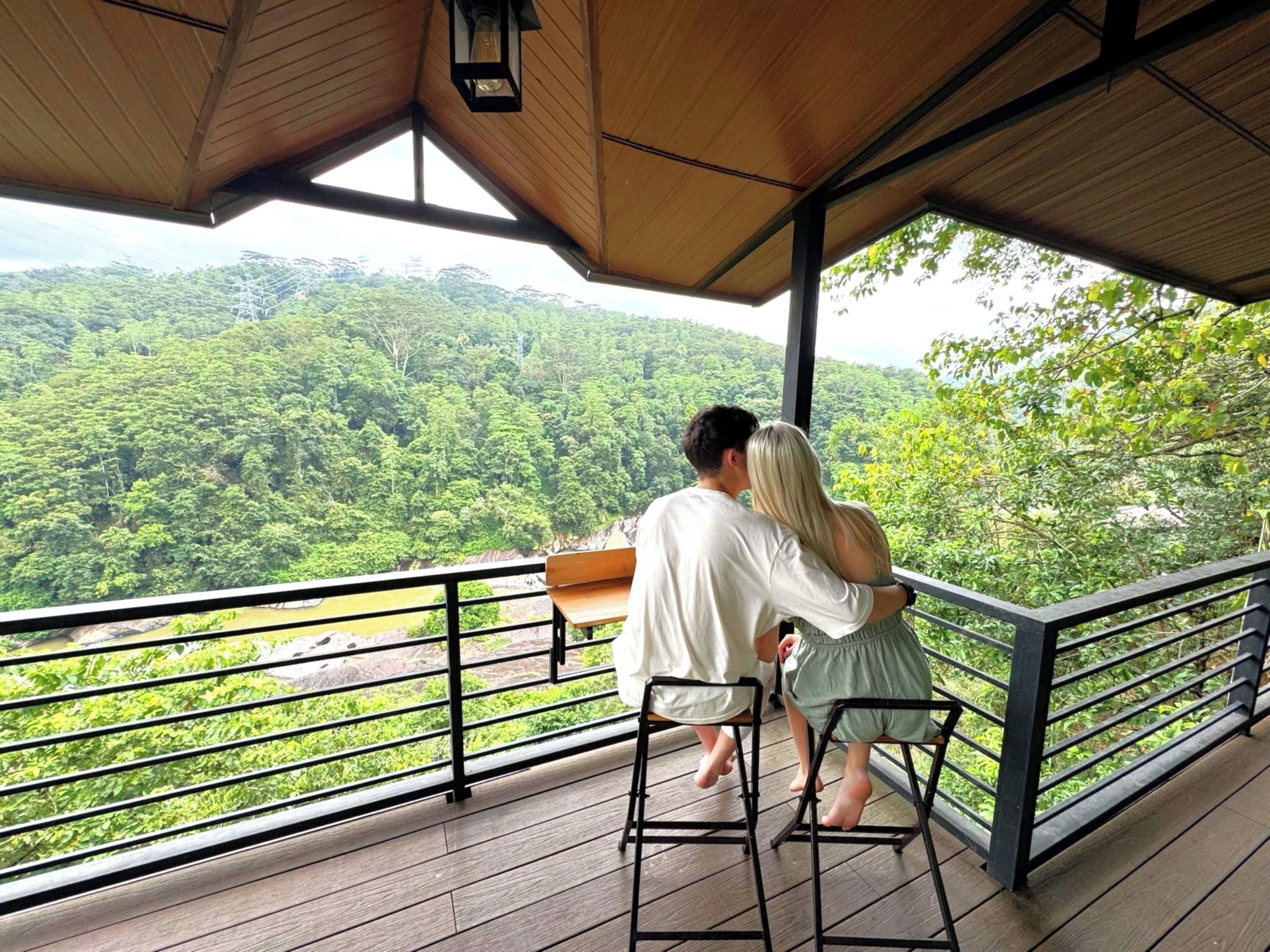 Una pareja abrazándose en una terraza de madera con vistas a un bosque frondoso.