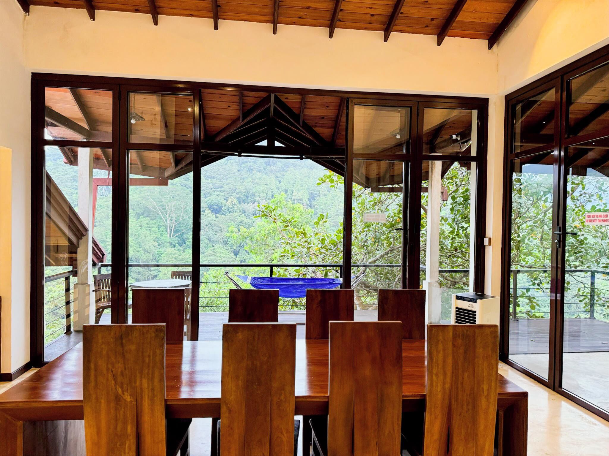 A dining area with a wooden table and chairs, large windows with a view of a forested landscape.