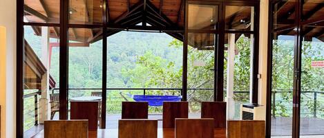 A dining area with a wooden table and chairs, large windows with a view of a forested landscape.