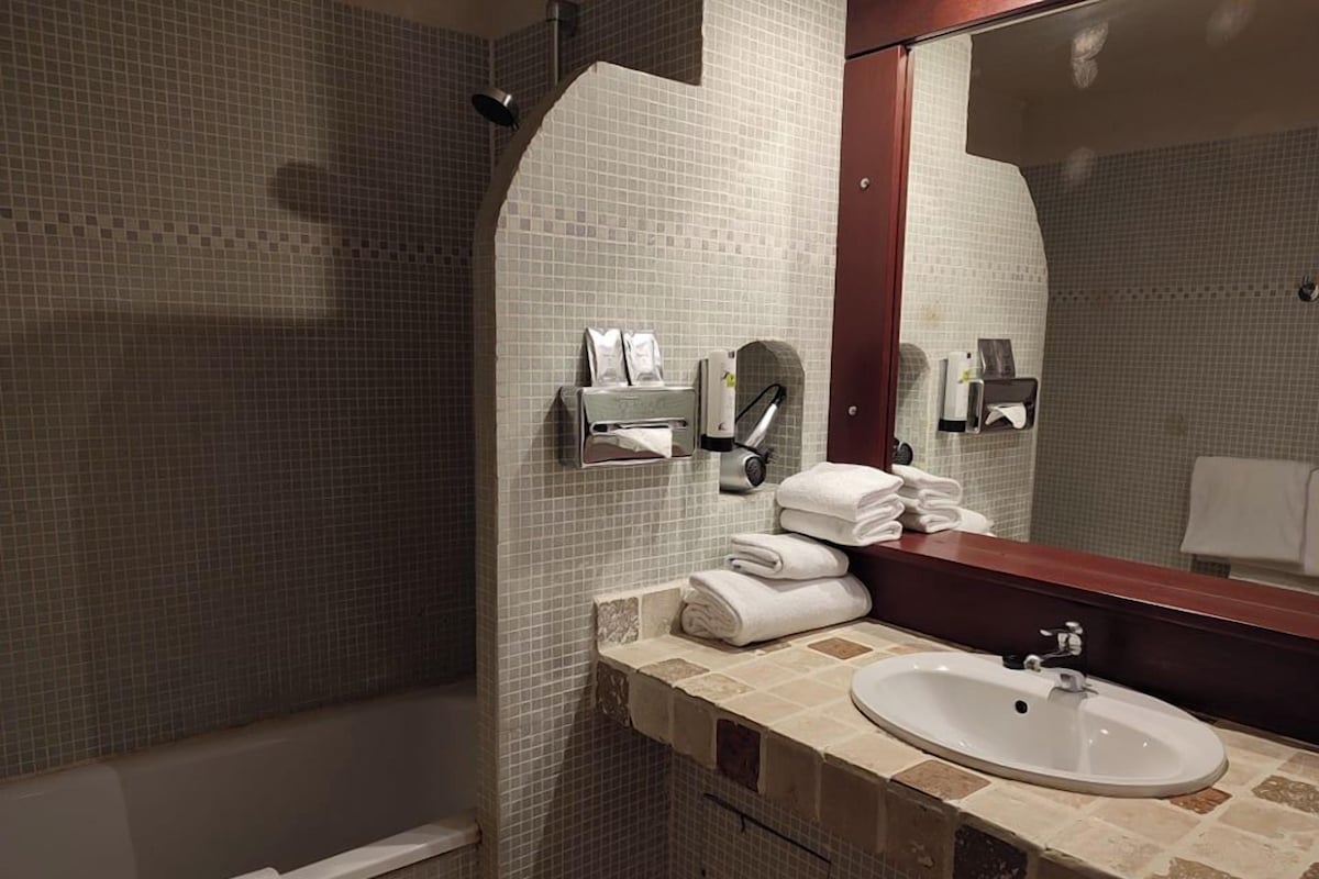 A bathroom with a tiled wall, a sink, a mirror, and a towel rack.