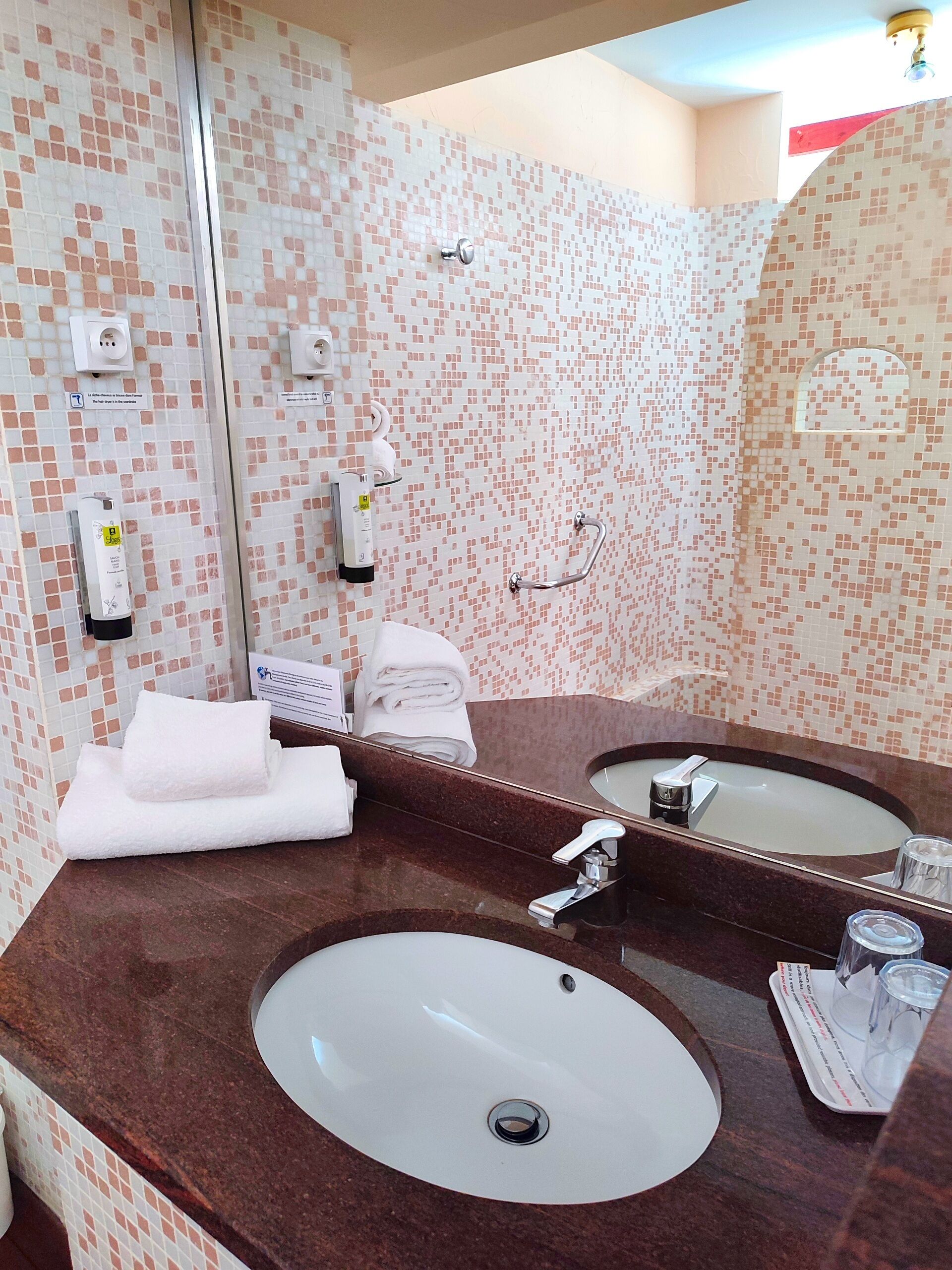 Ein Badezimmer mit großem Spiegel, zwei Waschbecken, einem Handtuchhalter und einer Duschkabine.