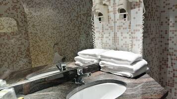 A bathroom with a granite countertop, a white sink, and a mirror. There are two towel dispensers on the wall and a stack of white towels on the counter.