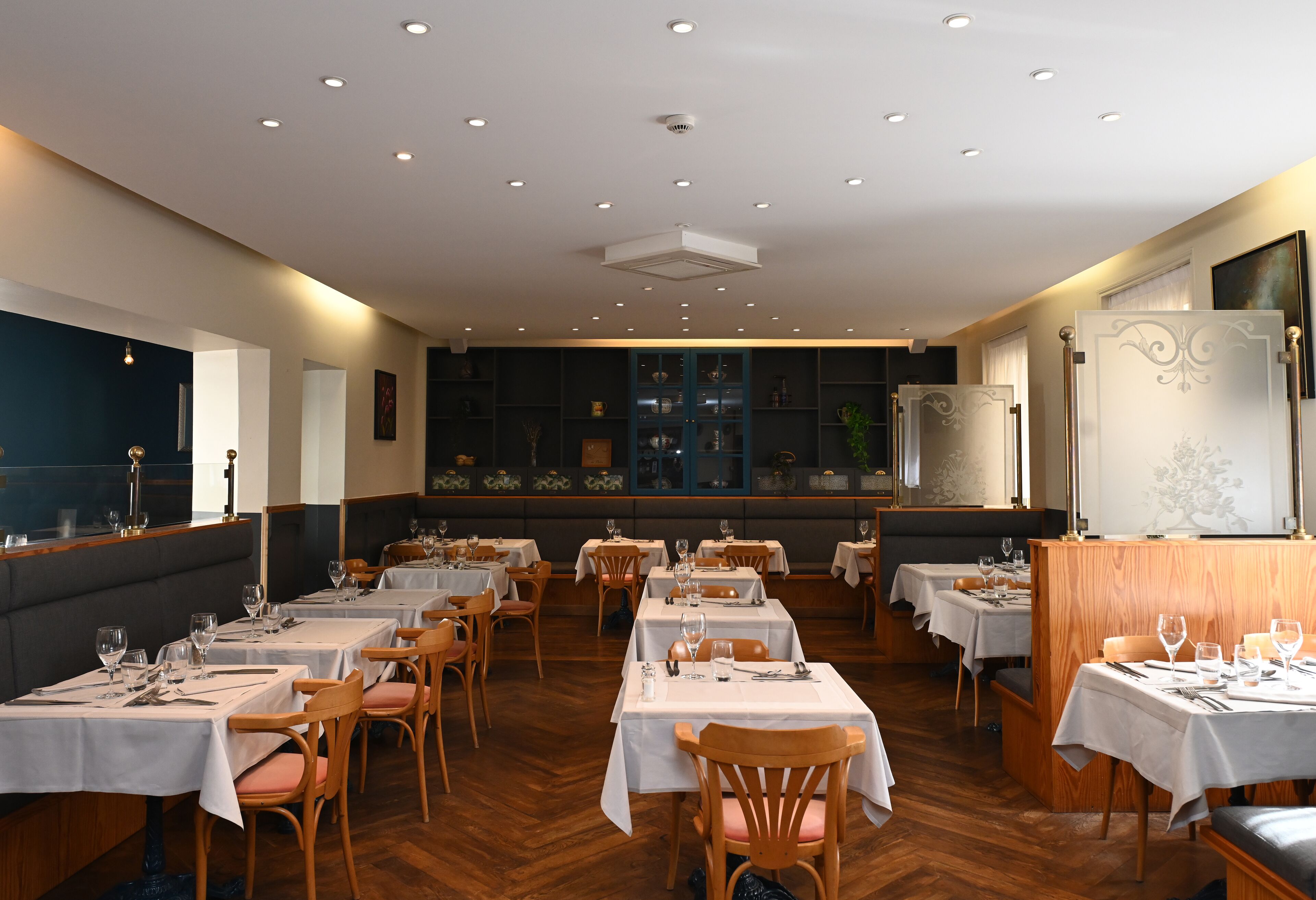 A restaurant with multiple tables and booths, wooden flooring, and recessed ceiling lights.