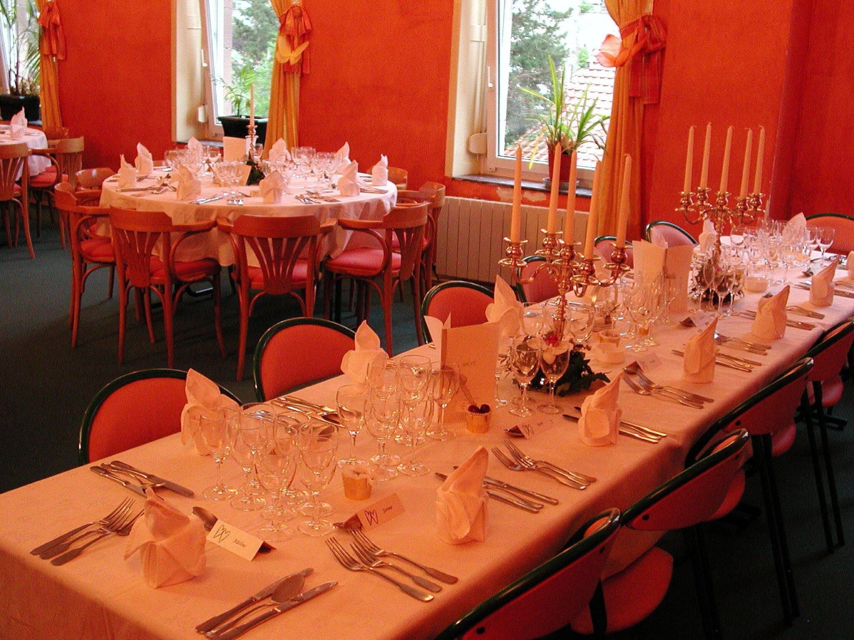 Uma sala de banquetes com mesas redondas preparadas para um evento formal, com toalhas brancas, copos e candelabros.