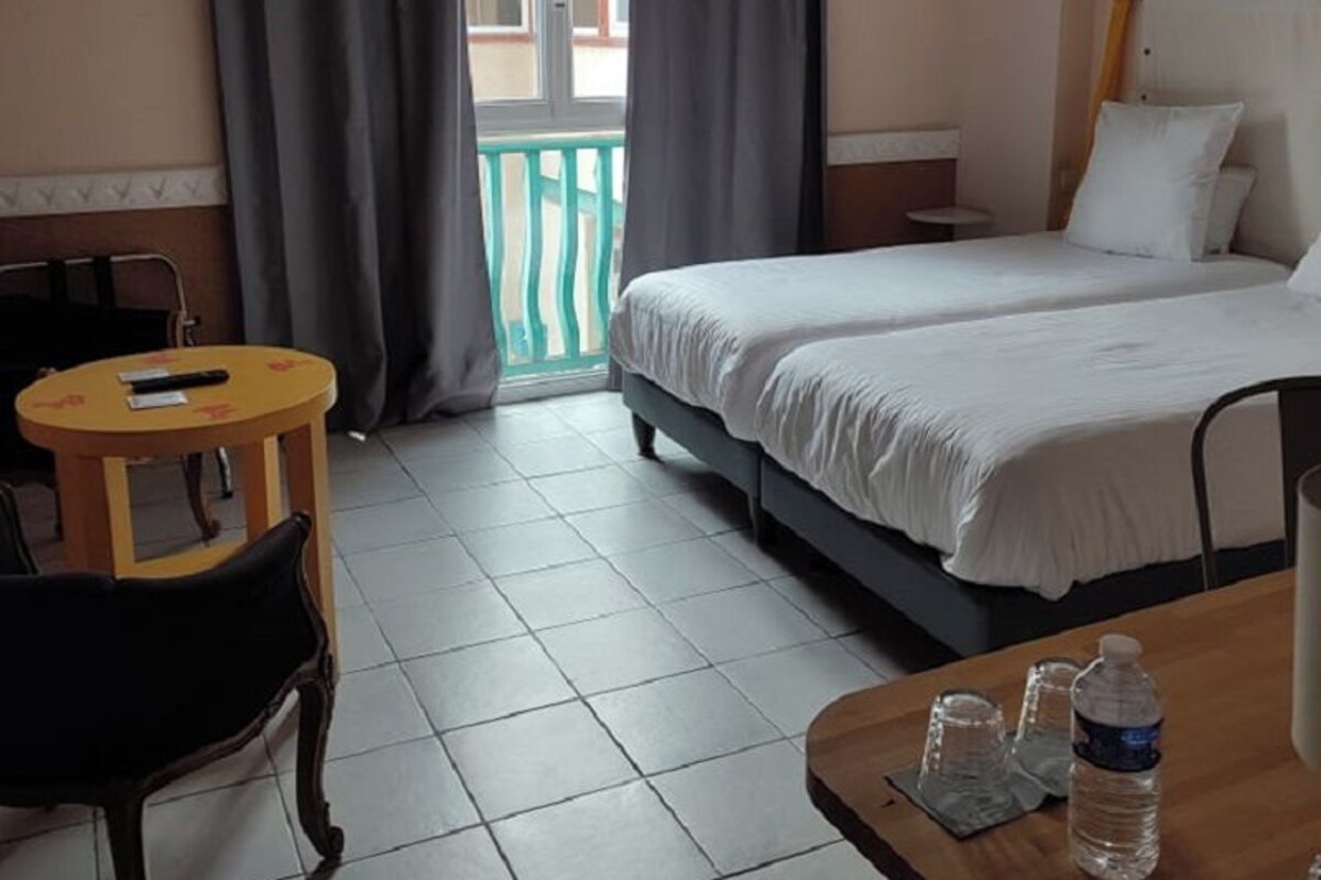 Een hotelkamer met een bed, een klein tafeltje met een stoel, een raam met gordijnen en uitzicht op buiten.