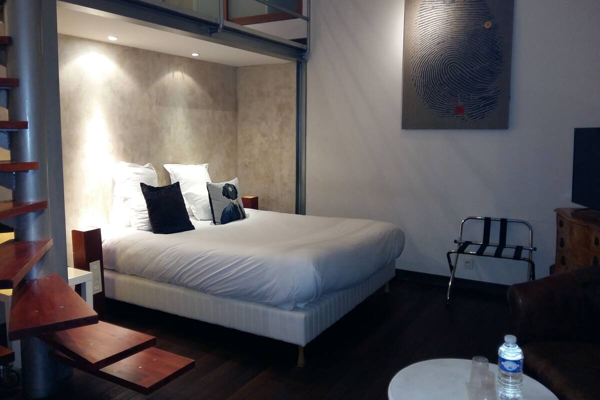 A modern bedroom with a bed, a painting of a fingerprint, a chair, and a water bottle on a table.