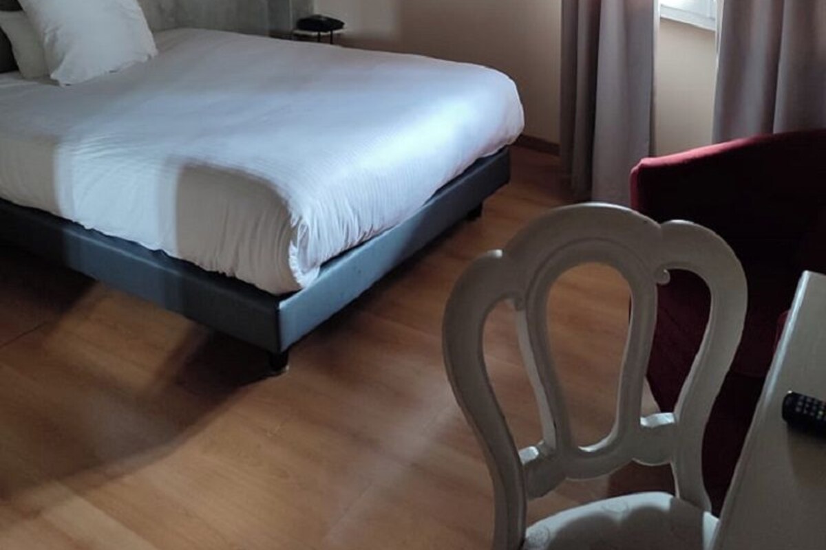 A bedroom with a bed, a chair, a desk, and a window with curtains.