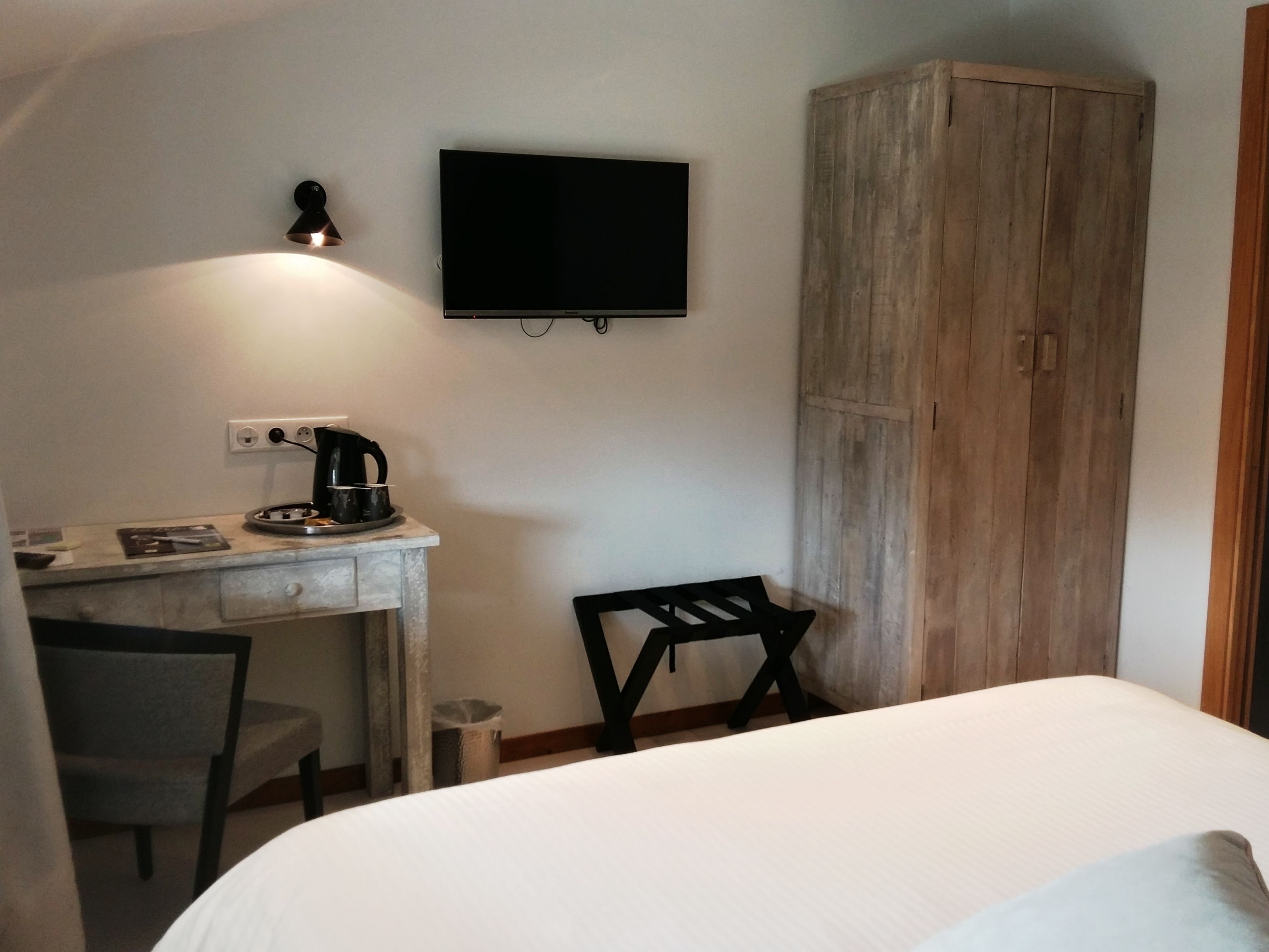 Un dormitorio con cama, escritorio con tetera, silla, televisor y armario.